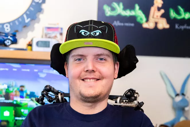 Dennis Winkens sitzt in seinem Zimmer und lächelt.