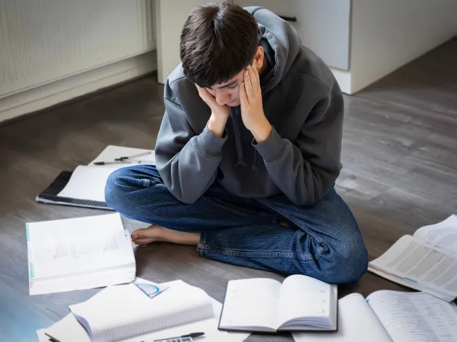 Junge sitzt müde zwischen Büchern auf dem Boden