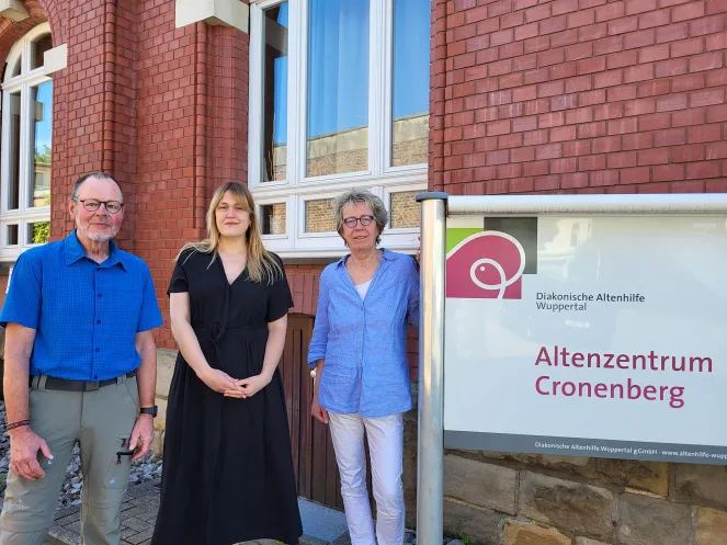 Ein Mann und zwei Frauen stehen an einem Schild vor einem Seniorenzentrum