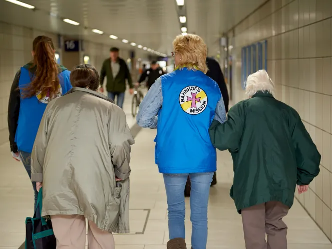 Mitarbeiterin der Bahnhofsmission mit zwei Menschen
