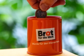 Eine Person steckt Geld in eine Spendendose von Brot für die Welt.