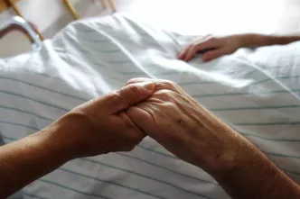 Händehalten bei einem älteren Menschen im Klinikbett