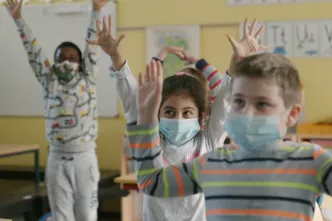 Kinder mit Masken strecken die Hände in die Höhe