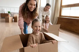 Kinder sitzen im Umzugskarton und werden von ihren Eltern angeschoben