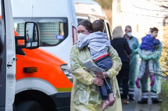 Eine Frau im gelben Schutzkittel trägt einen kleinen Jungen auf dem Arm