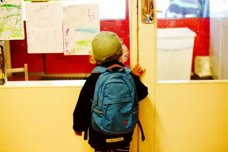 Junge mit Rucksack schaut durch eine Tür