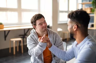 Mann mit Down-Syndrom schlägt in die Hand eines anderen Mannes ein.