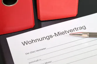 Mietvertrag und Kugelschreiber vor roten Aktenordnern.