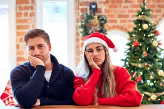 Ein junges Paar sitzt erschöpft und beleidigt vor dem Weihnachtsbaum.