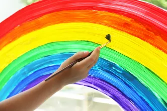 Kind malt einen Regenbogen an ein Fenster. (Foto: Shutterstock)
