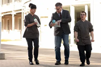 Gerhard Bröker (Mi.) mit zwei Mitarbeitenden in fair produzierter Kleidung.