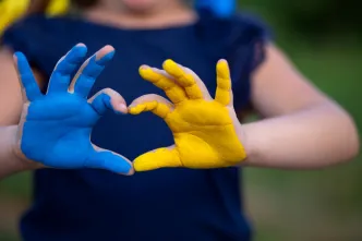 Eine Frau formt mit ihren Handflächen, die gelb und blau bemalt sind ein Herz als Zeichen der Solidarität mit der Ukraine.