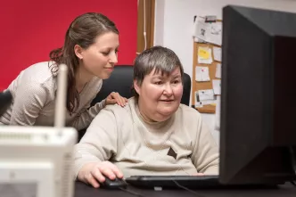 Betreuerin beugt sich über geistig behinderte Frau