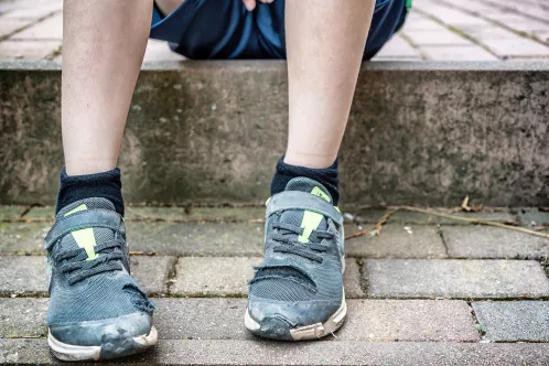 Ein Junge hat Turnschuhe mit Löchern an.